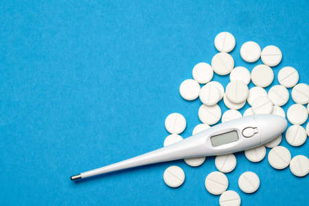 group of white pills or tablets and electronic digital thermometer on blue background