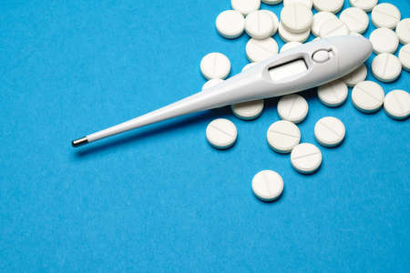 group of white pills or tablets and electronic digital thermometer on blue backgroundの写真素材