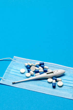 Protective medical face mask,Thermometer and pills on a blue background - Top view with copy space