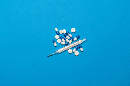 group of white pills or tablets and mercury thermometer on blue background