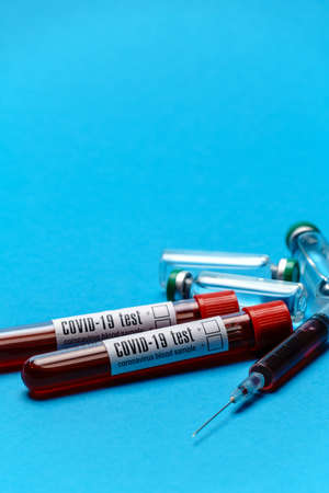 Syringe, test tubes with blood samples and ampoules with medicines or vaccine over blue background