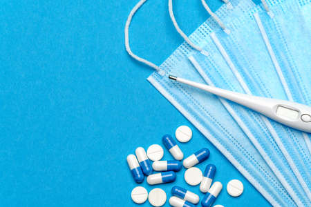 Protective medical face mask,Thermometer and pills on a blue background - Top view with copy space