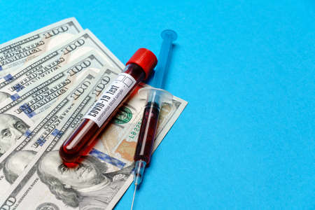 Close up 100 US dollar bills and blood sample in test tube over blue background