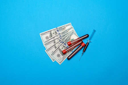 Close up 100 US dollar bills and blood sample in test tube over blue backgroundの写真素材