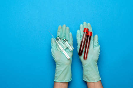lab technician assistant or doctor wearing rubber or latex gloves holding an ampoule with medicine or vaccine and test tube with blood sampleの写真素材