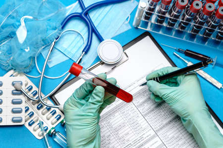 lab technician assistant or doctor wearing rubber or latex gloves holding blood test tube over clipboard with blank formの写真素材