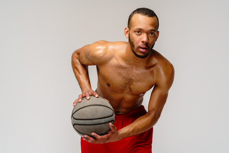 Muscular african american sportsman playing basketball shitless over light grey backgroundの写真素材