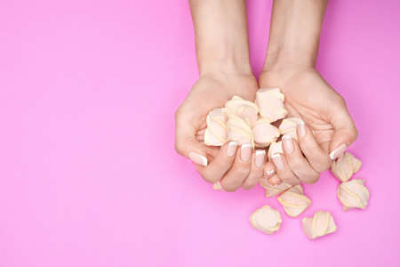 Beautiful Female Hands with French manicure and marshmallows over colorful pink paper backgroundの写真素材