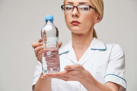 Portrait of young caucasian woman health care professional holding bottle of water standing over light grey backgroundの写真素材