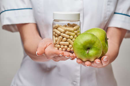 nutritionist doctor healthy lifestyle concept - holding organic fresh green apple and can of vitamin capsulesの写真素材