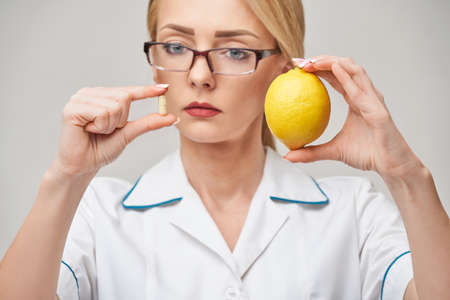 nutritionist doctor healthy lifestyle concept - holding fresh organic lemon fruit and vitamin capsulesの写真素材