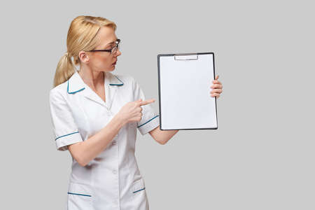 beautiful female doctor holding clipboard isolated on grey backgroundの写真素材