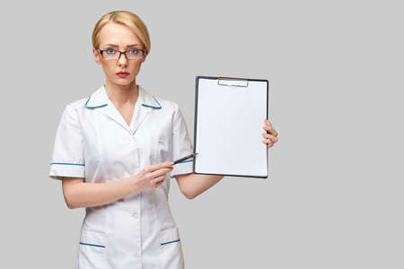 beautiful female doctor holding clipboard isolated on grey backgroundの写真素材