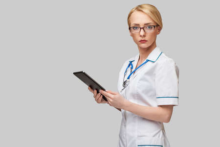 beautiful female doctor holding tablet pc pad isolated on grey backgroundの写真素材
