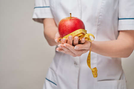nutritionist doctor healthy lifestyle concept - holding organic red apple and measure tapeの写真素材