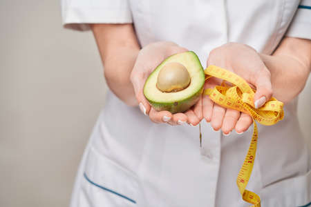 nutritionist doctor healthy lifestyle concept - holding organic avocado fruit and measure tapeの写真素材