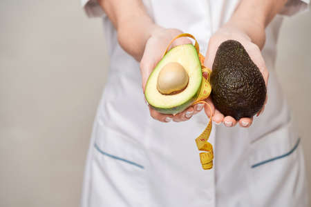 nutritionist doctor healthy lifestyle concept - holding organic avocado fruit and measure tapeの写真素材