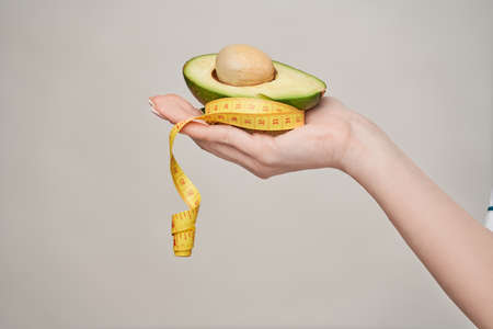 nutritionist doctor healthy lifestyle concept - holding organic avocado fruit and measure tapeの写真素材