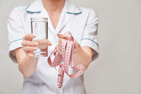 Healthy eating or lifestyle concept - female woman doctor holding and a glass of clear fresh water and measure tapeの写真素材