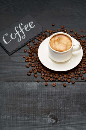 stone serving board with chalk handwritten sign, cup of espresso and coffee beans on dark wooden backgroundの写真素材
