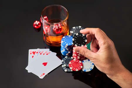 Casino chips, playing cards, glass of whiskey and dices on dark reflective background