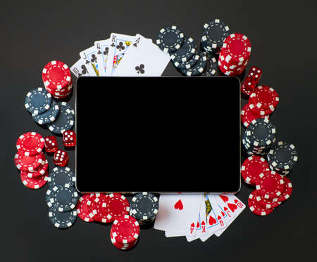 Casino chips, playing cards, dices and tablet pc pad on dark reflective backgroundの写真素材