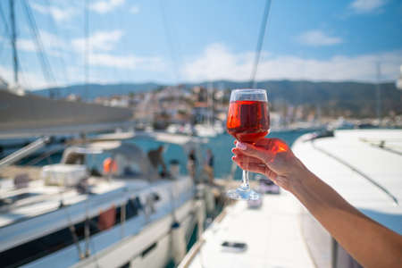 Woman holding glass of wine against yachts at the harbor of Poros. Greeceの写真素材