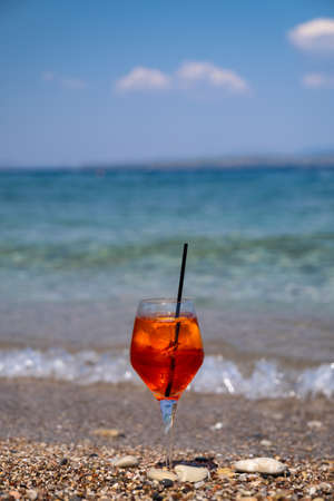 glass of aperol spritz cocktail stands on sand near the seaの写真素材