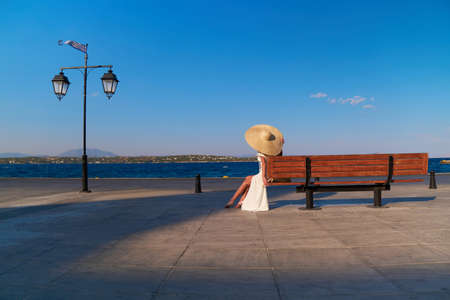 Woman in sun straw hat sitting on a wooden bench at Spetses marina, Greece