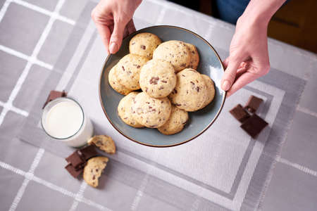 woman holding Chocolate chip cookie on ceramic plate at domestic kitchen
