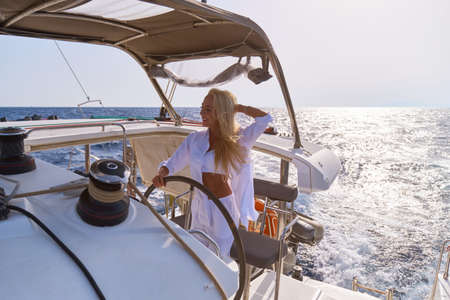beautiful woman standing on yacht captains bridge at sunny summer dayの写真素材