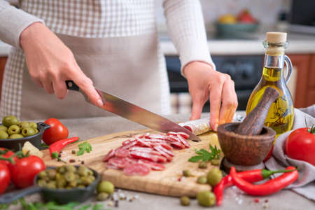 Woman slicing Spanish sausage fuet salami with knife on a domestic kitchenの写真素材