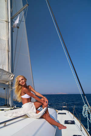Beautiful young blond woman in bikini sitting on catamaran at sunny summer day