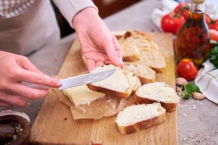 Woman spreading tasty organic butter onto bread over grey table with wooden cutting board