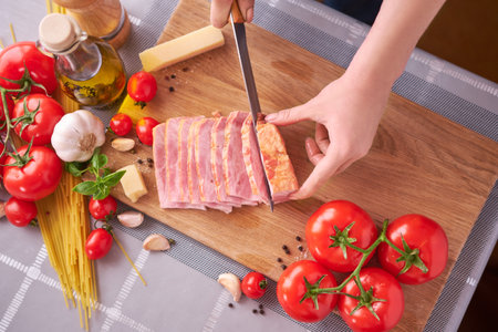 womans hands slicing pancetta ham bacon on wooden cutting board at domestic kitchen