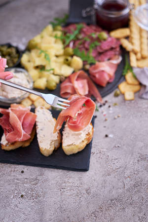 Woman holding piece of prosciutto ham on a fork standing at domestic kitchenの写真素材