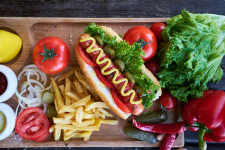 BBQ hot dog served with vegetables and French fries and sauces on wooden serving board