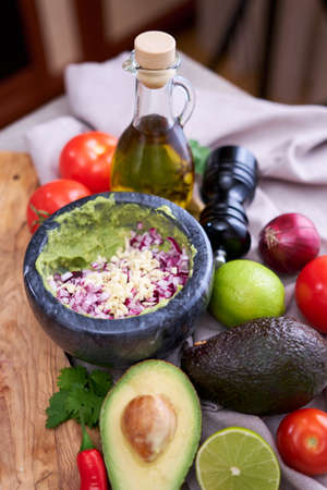 making guacamole - crushed avocado in marble mortar and ingredients