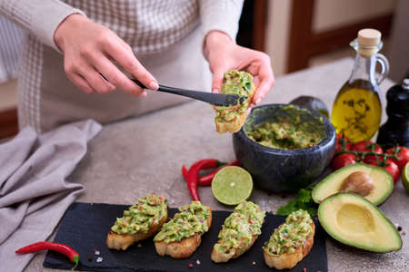woman making bruschetta with freshly made guacamole on domestic kitchenの写真素材
