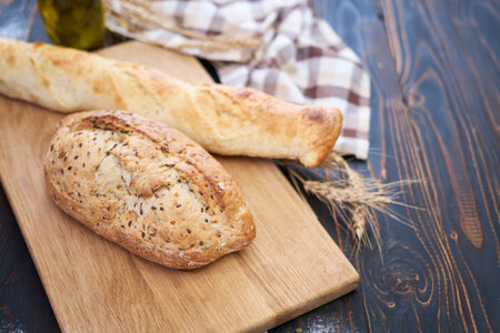 Fresh bread loaf and baguette on wooden cutting board at kitchen tableの写真素材