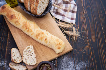 Fresh baguette and sliced bread on wooden cutting board at kitchen table