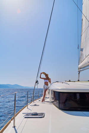 Beautiful young blond woman in bikini standing on catamaran at sunny summer day
