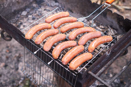 Tasty Sausages grilling on charcoal grill grate