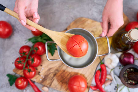 woman blanching a tomato holding over pan with hot water for further peelingの写真素材