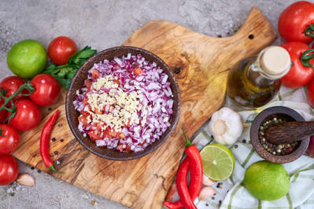 making salsa dip sauce - chopped garlic, tomatoes and onion in wooden bowlの写真素材