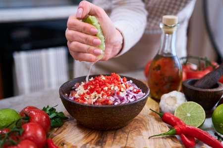 making salsa dip sauce - woman squeezing fresh lime juice to chopped ingredients in wooden bowlの写真素材