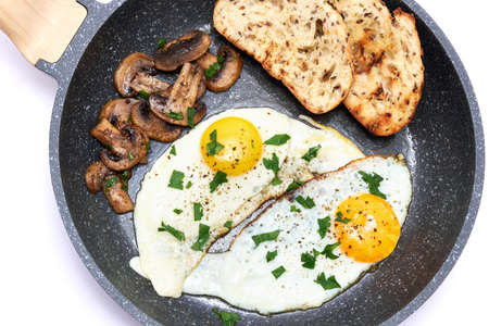 Close up view of the fried egg, bread and mushrooms on a frying pan isolated on white background