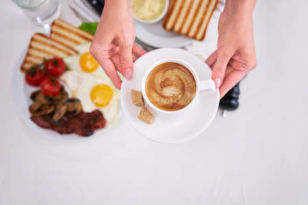 Fried eggs, bacon, tomato, toasted bread in white ceramic plate and cup of coffeeの写真素材