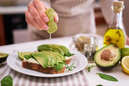 Woman squeezing fresh lime juice on a Avocado and cream cheese toastsの写真素材
