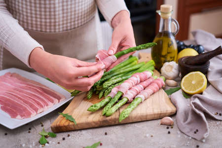 woman cooking green aspargus covered with bacon at domestic kitchenの写真素材